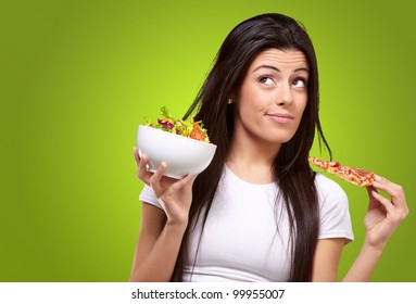 portrait of a young woman choosing pizza over salad against a green background - Powered by Shutterstock