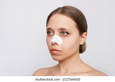Portrait of a young woman with cleaning nose strips from blackheads or black dots on her skin isolated on a gray background. Acne problem, comedones. Enlarged pores on the face. Cosmetology concept