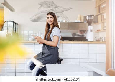 Portrait Of Young Woman Coffee Brew Master Starting Her Day With A Social Network In A Bright Caffee. Barista Is Her Dream Job.