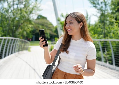 Portrait Of Young Woman With Comfortable Clothes Typing With Finger On Mobile Phone On City Park. Sustainable Eco-friendly City And Lifestyle Technology Concept.