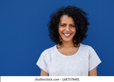 Portrait Of A Young Woman With Curly Brown Hair Standing Against A Colorful Blue Background And Smiling