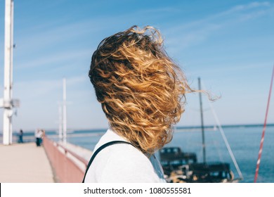 Portrait of a young woman with curly hair on the beach on a windy day