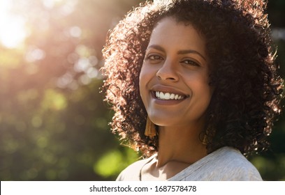 Portrait Of A Young Woman With Curly Hair Standing Outside In A Park And Smiling On A Sunny Summer Afternoon