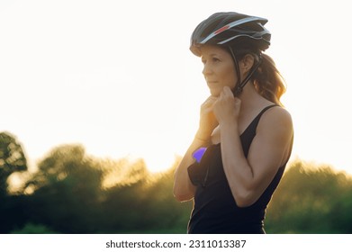 Portrait of a young woman cyclist adjusting her helmet while preparing for riding road bicycle on a free road in the forest at a sunny day. Healthy lifestyle concept. Copy space. - Powered by Shutterstock