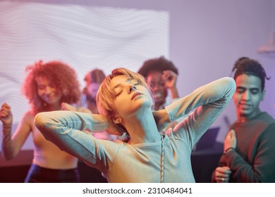 Portrait of young woman dancing with eyes closed in nightclub and enjoying mucis with crowd in background - Shutterstock ID 2310484041