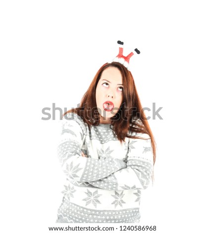 Portrait of a young woman doing a silly face while wearing a headband with Santa's legs and a Christmas jumper against a white background