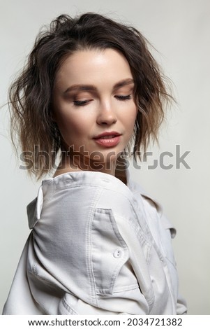Portrait of young woman with downcast eyes. Female posing in milky white micro-corduroy shirt.