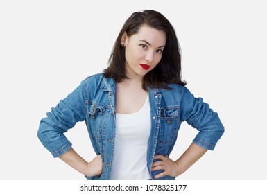 Portrait of a young woman dressed in jeans jacket standing with arms akimbo. Isolated on a white background. Look at camera.