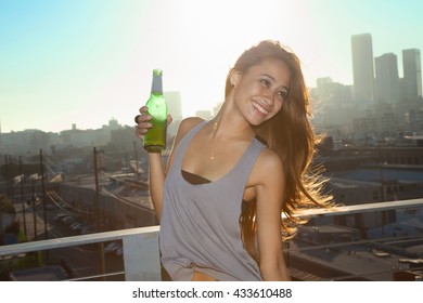 Portrait Of Young Woman Drinking Beer On Rooftop Bar With Los Angeles Skyline, USA