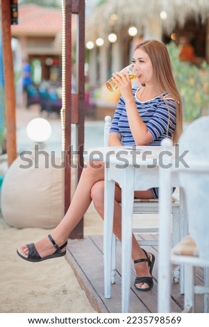 Portrait of a young woman drinking beer on the terrace of a beach cafe on a summer sunny day