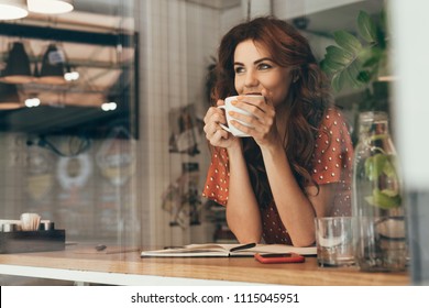 portrait of young woman drinking coffee at table with notebook in cafe