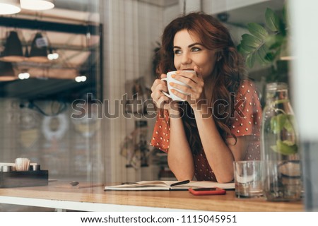 portrait of young woman drinking coffee at table with notebook in cafe
