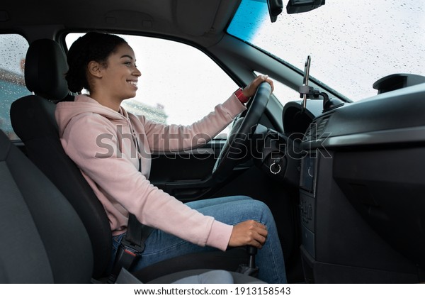Portrait of young woman driver relaxing enjoy trip\
with friend. Cheerful millennial african american lady sits in car,\
changes gears and looks at city road, view from passenger seat,\
copy space