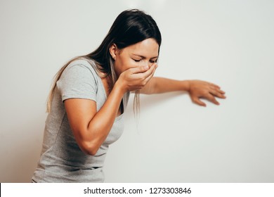 Portrait of young woman drunk or sick vomiting over gray background