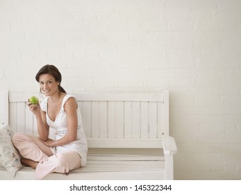 Portrait Of A Young Woman Eating Apple On Bench