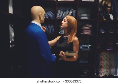 Portrait Of Young Woman Entrepreneur Straightens Tie On Mannequin While Standing With Touch Pad In Her Store,beautiful Female Seller Using Digital Tablet For Checks The Stock Number Of Clothes In Shop