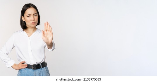 Portrait Of Young Woman Extending One Hand, Stop Taboo Sign, Rejecting, Declining Something, Standing Over White Background