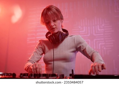 Portrait of young woman as female DJ making music tracks at disco party in neon light - Shutterstock ID 2310484057