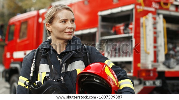Portrait of young woman firefighter standing near fire\
truck. 