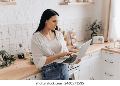 Portrait of young woman freelancer or student working on a laptop in her kitchen, taking breaks between household chores or cooking. Perfect for content about balancing education, work, and home life - Powered by Shutterstock