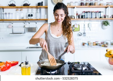Portrait of young woman frying onion into the pan in the kitchen.