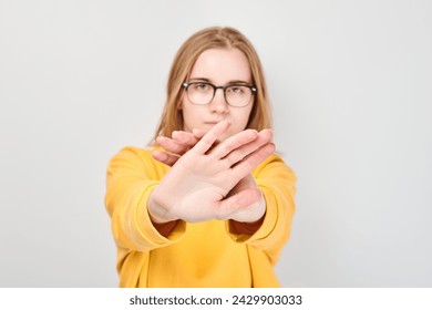 Portrait of young woman in glasses making stop gesture with her hands against grey background - Powered by Shutterstock