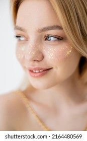 Portrait of young woman with glitter visage looking away isolated on grey