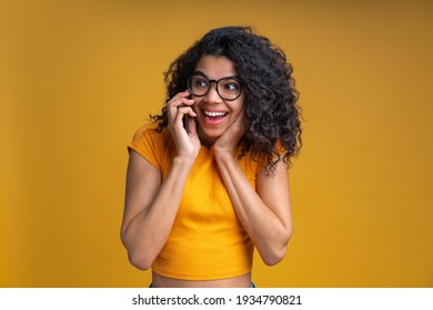 Portrait Of Young Woman Gossiping On Her Mobile Phone. Portrait Of Smiling Girl Talking To Her Friends On Smartphone Isolated Over Yellow Background.