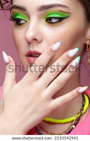 Portrait of young woman with hand near face. Female with unusual green eyes shadows makeup. Girl with nails with multi-colored manicure.