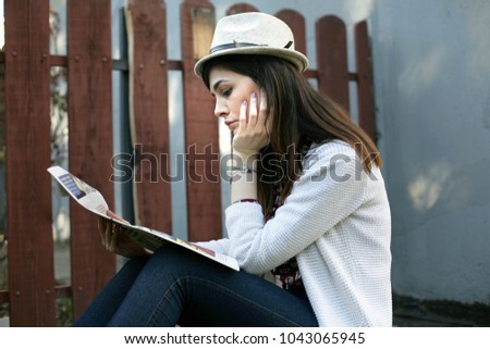 Portrait of a young woman; woman with hat is reading newspaper outdoors.