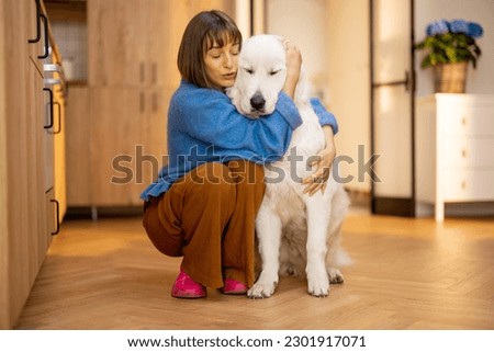 Portrait of young woman with her huge white dog, hugging together at home. Concept of domestic lifestyle and friendship with pets. Maremma shepherd dog