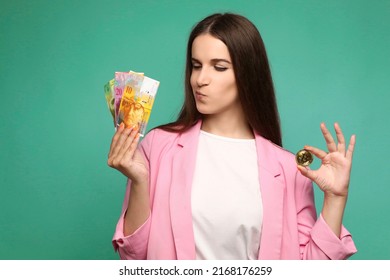 Portrait of young woman holding bitcoin and swedish krona banknotes and looking thoughtfully at swedish krona