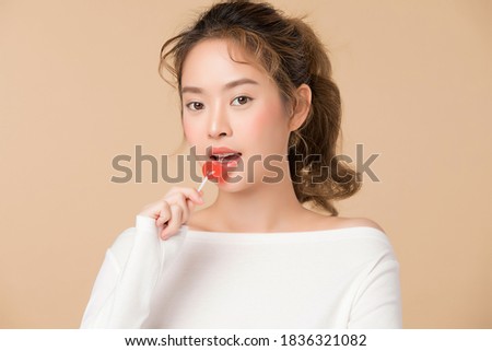 Portrait of young woman holding a candy in heart shape isolated on beige color background