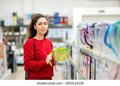 Portrait of young woman holding a light green carafe with a water filter in a store. The concept of consumerism.