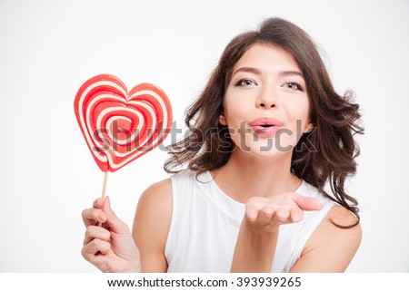 Portrait of a young woman holding lollipop and blowing kiss at camera isolated on a white background