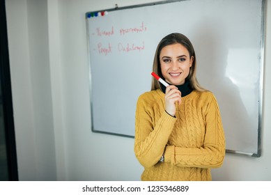 Portrait Of A Young Woman Holding Marker While Standing In Front Of Whiteboard.