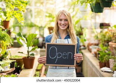 Portrait of young woman holding open sign placard at greenhouse - Powered by Shutterstock