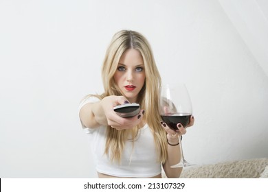 Portrait of a young woman holding wine glass while using remote control