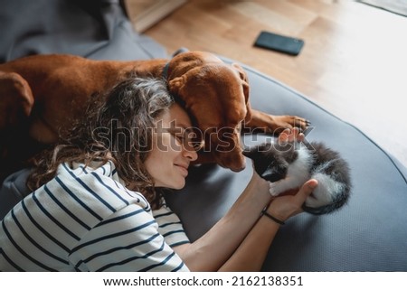 Portrait of a young woman with a Hungarian Pointer dog and a small kitten in her arms lying at home
