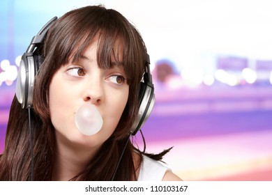 portrait of young woman listening to music with bubble gum over abstract background