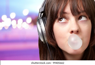 portrait of young woman listening to music with bubble gum over abstract lights