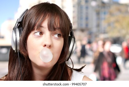 portrait of young woman listening to music with bubble gum at crowded street