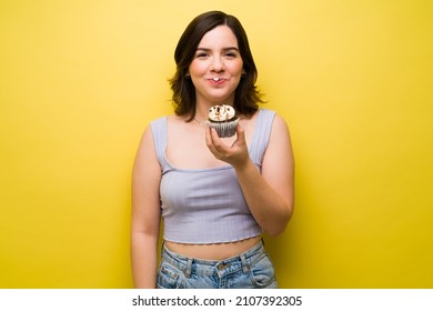 Portrait Of A Young Woman Looking At The Camera And With Sugar Icing On Her Face Eating A Cupcake 