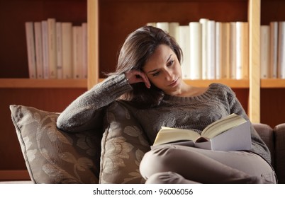 Portrait Of A Young Woman Lying On Couch With Book