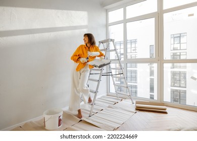 Portrait of a young woman making repairing in apartment, standing with paint roller near ladder in bright room of her new home - Powered by Shutterstock