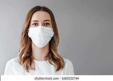 Portrait of a young woman in a medical mask isolated over grey background. Young girl patient stands against the wall background, copy space for text