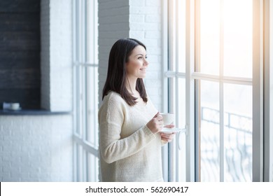 Porträt von jungen Frauen in der Nähe des Fensters mit einer Tasse Tee oder Kaffee. Träumen und entspannen