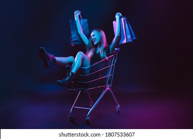 Portrait of young woman in neon light on dark backgound with shopping bags, black friday