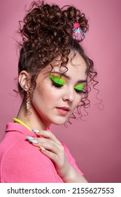 Portrait of young woman on pink background. Female with unusual green eyes shadows makeup, curly hair and earrings. - Shutterstock ID 2155627553