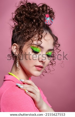 Portrait of young woman on pink background. Female with unusual green eyes shadows makeup, curly hair and earrings.